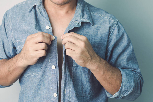 Falscher erster Knopf, der Rest ist falsches Konzept. Mann knöpft blaues Jeanshemd zu. Studioaufnahme auf grauem Wandhintergrund. - Foto, Bild