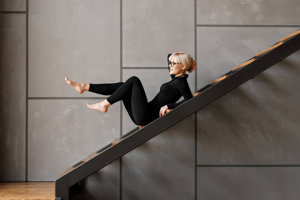 Sexy blonde girl in a black fitted suit, looking at the camera. Concept of fashion, yoga. - 写真・画像