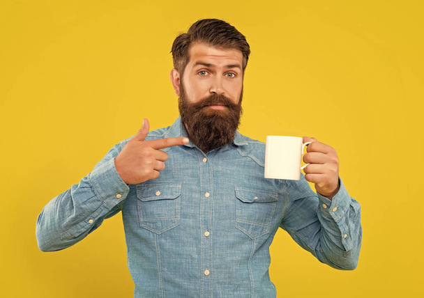 Serious man pointing finger at coffee mug yellow background, copy space. - Photo, image