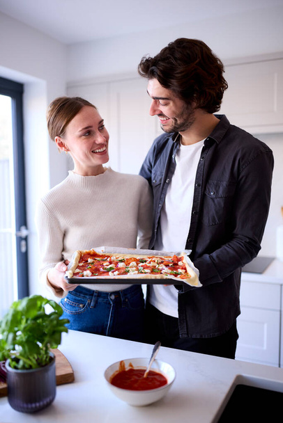 Couple In Kitchen At Home With Homemade Pizza Ready To Be Baked In Oven - 写真・画像