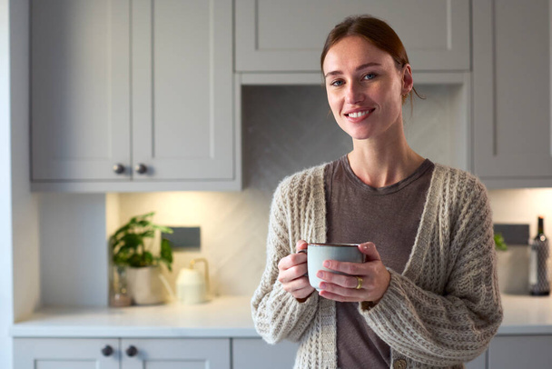 Portrait Of Young Woman Relaxing At Home In Kitchen Holding Hot Drink - Fotoğraf, Görsel