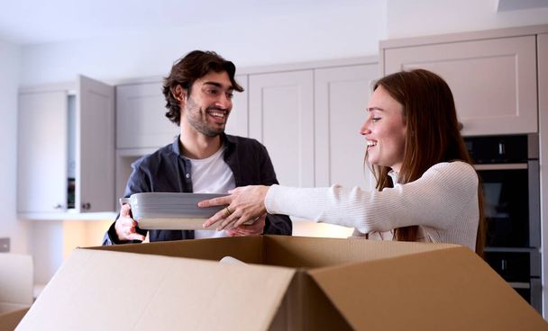 Young Couple Moving Into New Home Unpacking Boxes In Kitchen Together - Foto, imagen