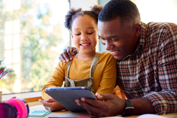 自宅でデジタルタブレットを使って宿題をしている娘を助けるお父さん - 写真・画像