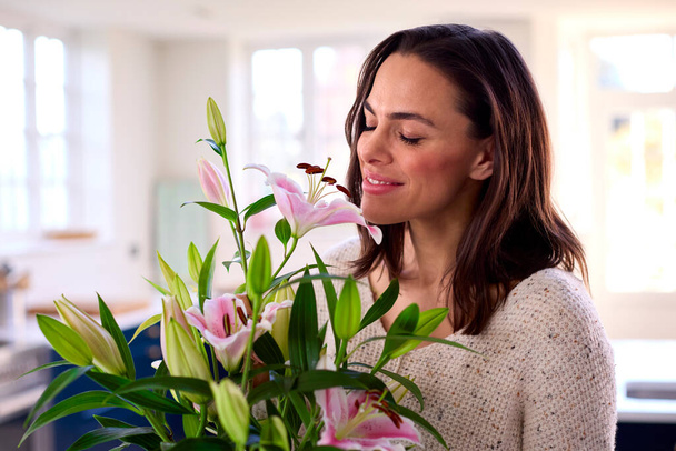 Smiling Woman At Home Smelling And Arranging Bouquet Of Flowers In Glass Vase - Φωτογραφία, εικόνα