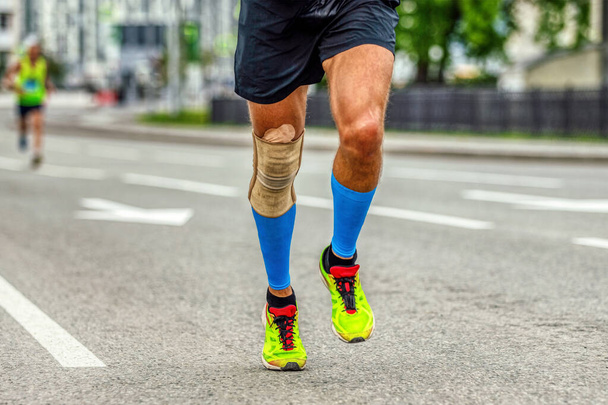 piernas hombre corredor en rodilleras y calcetines de compresión corriendo maratón, manga de la rodilla de protección después de la lesión a la estabilización - Foto, Imagen