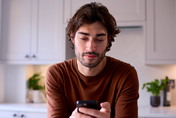 Young Man Relaxing At Home In Kitchen Checking Messages Social Media On Mobile Phone - Photo, Image