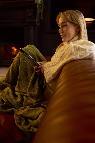 Woman At Home In Lounge With Cosy Fire Using Or Watching Digital Tablet - Photo, Image