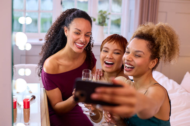 Skupina ženských přátel doma oblečené a pití šampaňské pózování pro selfie před nocí - Fotografie, Obrázek