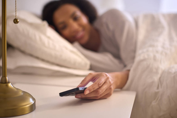 Woman At Home In Bed Turning Off Alarm On Mobile Phone - Foto, imagen