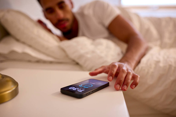 Man At Home In Bed Turning Off Alarm On Mobile Phone - Фото, зображення