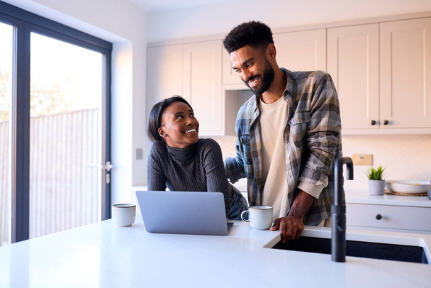 Young Couple At Home Looking At Laptop On Counter In Kitchen Together - Foto, Imagem