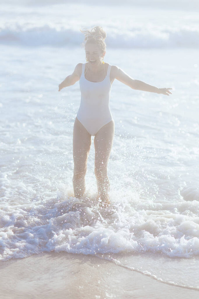 Full length portrait of happy modern middle aged woman in white beachwear at the beach having fun time. - Foto, imagen
