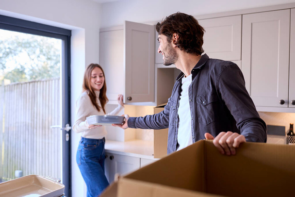 Young Couple Moving Into New Home Unpacking Boxes In Kitchen Together - Foto, Imagen
