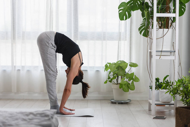 Молодая женщина практикует йогу дома. Дневные занятия спортом для здорового образа жизни и снятия стресса. - Фото, изображение