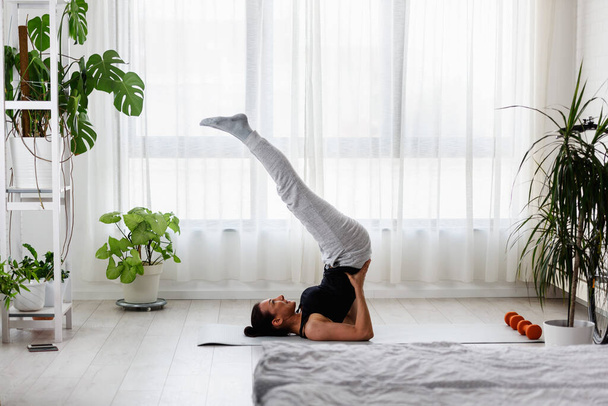 Junge Frau praktiziert Yoga-Übungen zu Hause. Sportliche Tagesabläufe für einen gesunden Lebensstil und Stressabbau. - Foto, Bild