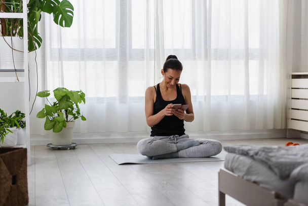 Jovem mulher esportiva usando smartphone após o exercício em casa - Foto, Imagem