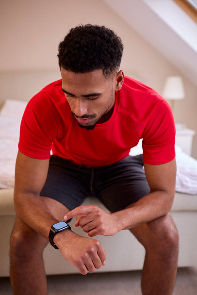 Young Man In Bedroom At Home In Fitness Clothing Checking Fitness App On Smart Watch Before Exercise - Foto, Bild