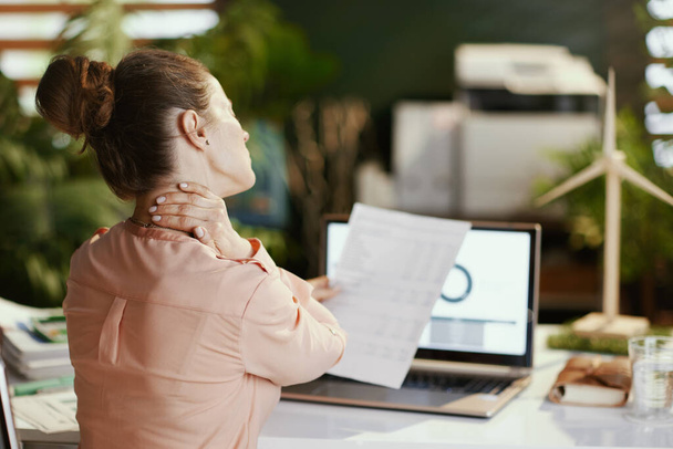 Seen from behind modern business woman with documents and laptop having neck pain in modern office. - Foto, imagen