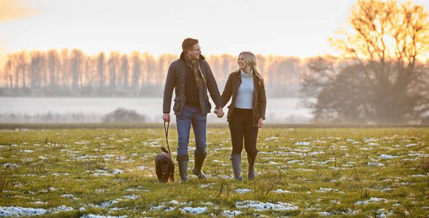 Loving Couple With Pet Spaniel Dog On Snowy Walk In Winter Countryside - Foto, afbeelding