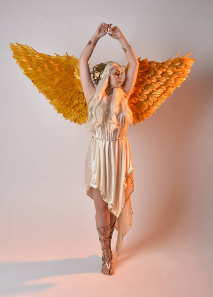 Retrato de larga duración de una hermosa mujer rubia con un disfraz de toga de diosa de fantasía con alas de ángel emplumadas. Saltando posan como volando, aislados sobre fondo blanco del estudio. - Foto, imagen