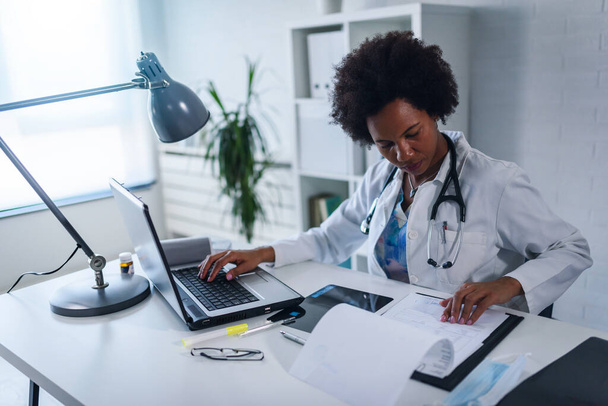 Medico donna che lavora nel suo ufficio di fronte al computer portatile, scrivendo un rapporto sullo stato di salute - Foto, immagini