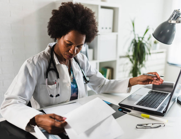 Ärztin sitzt in ihrem Büro vor dem Laptop und schreibt einen Gesundheitsbericht - Foto, Bild