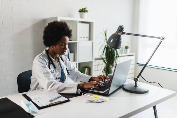 Ärztin sitzt in ihrem Büro vor dem Laptop und schreibt einen Gesundheitsbericht - Foto, Bild