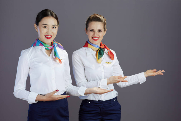 smiling elegant female stewardesses in blue skirt, white shirt and scarf welcoming isolated on grey background. - Fotó, kép
