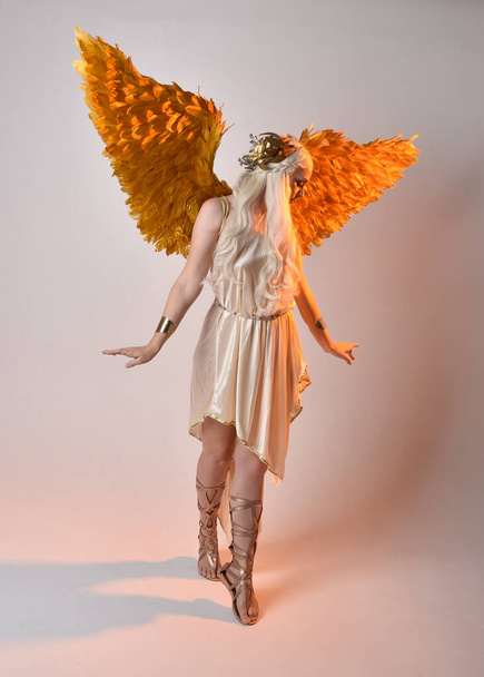 Volledig portret van een mooie blonde vrouw in een fantasie godin toga kostuum met gevederde engelenvleugels. Springen pose als vliegen, geïsoleerd op witte studio achtergrond. - Foto, afbeelding