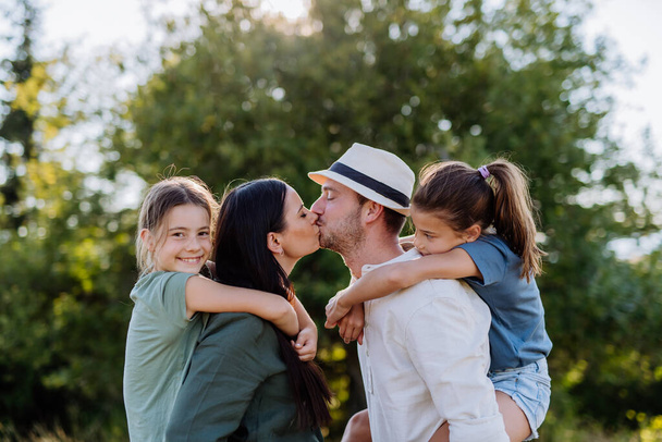 Portrait of young couple with their daughters in nature, kissing. Side view. - Foto, afbeelding