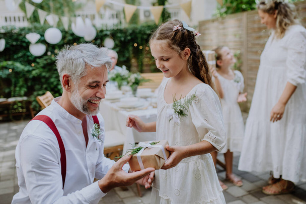A mature father groom receiving gift from his daughter at wedding reception outside in the backyard. - Photo, image
