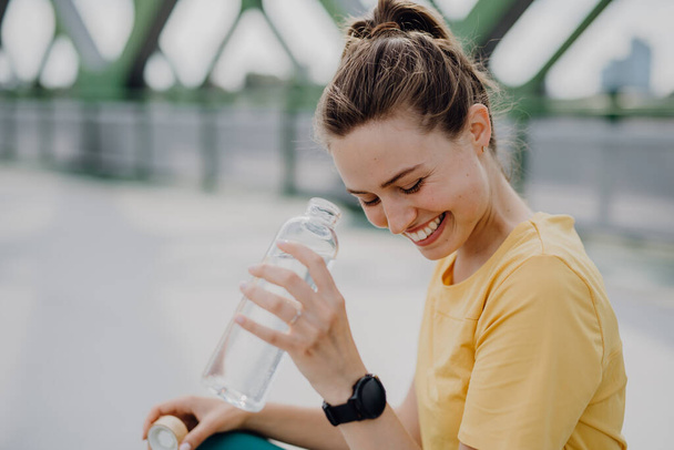 Young woman drinking water during jogging in a city, healthy lifestyle and sport concept. - Φωτογραφία, εικόνα