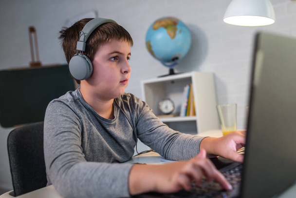 Концентрований серйозний хлопчик використовує ноутбук, сидячи на столі вдома. Технології, освіта, концепція дистанційного навчання
 - Фото, зображення