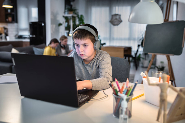 Keskittynyt vakava poika käyttää kannettavaa tietokonetta istuessaan pöydällä kotona. Teknologia, koulutus, etäopiskelu - Valokuva, kuva