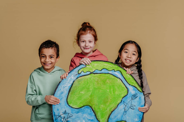 Portrait of three children with model of Earth, studio shoot. Concept of diversity in a friendship. - Fotó, kép