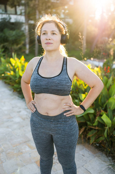 Fat woman and sports. Girl doing exercise for weight loss in the fresh air and laughing in camera after training. - Photo, Image