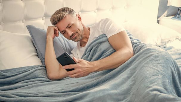 cheerful mature man in bed chatting on phone. - Valokuva, kuva