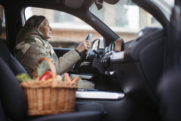 Mujer mayor conduciendo un coche, regresando de una tienda de comestibles. - Foto, imagen