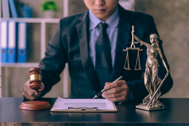 Ασιάτης νεαρός δικηγόρος που εργάζεται με φορητό υπολογιστή και σφυρί με κλίμακες που παρέχουν διαδικτυακές νομικές συμβουλές εξηγώντας τους κανόνες της σύμβασης στον νομικό σύμβουλο και την έννοια του γραφείου δικαιοσύνης - Φωτογραφία, εικόνα