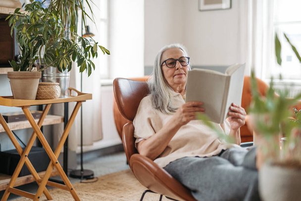 Senior woman reading a book, enjoying time alone in her apartment. - Photo, image