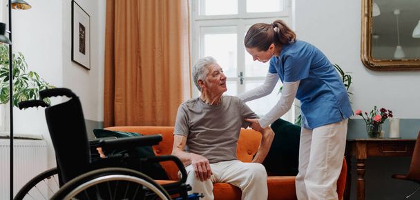 Young nurse helping senior man to stand up from a sofa. - 写真・画像