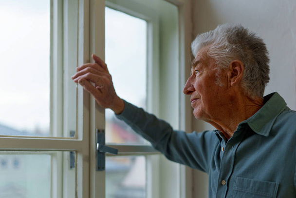 Senior man looking out of a window, concept of solitude in retirement. - Valokuva, kuva