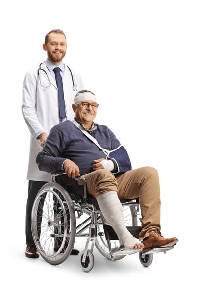 Mature man with a broken arm and bandage on head sitting in a wheelchair and a doctor standing behind isolated on white background - Foto, imagen