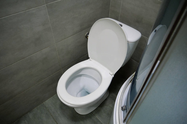 Toilettenraum innen mit weißer Toilettenschüssel, Duschkabine und grauen Wandfliesen - Foto, Bild