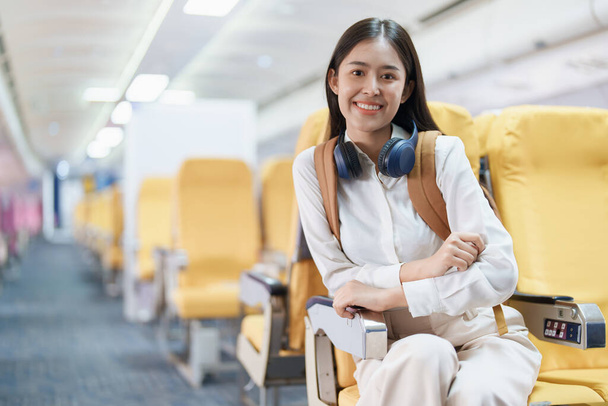 Jonge Aziatische aantrekkelijke vrouw reizen per vliegtuig, Passagier het dragen van een koptelefoon zetten handbagage in kluisjes boven stoelen van het vliegtuig. - Foto, afbeelding