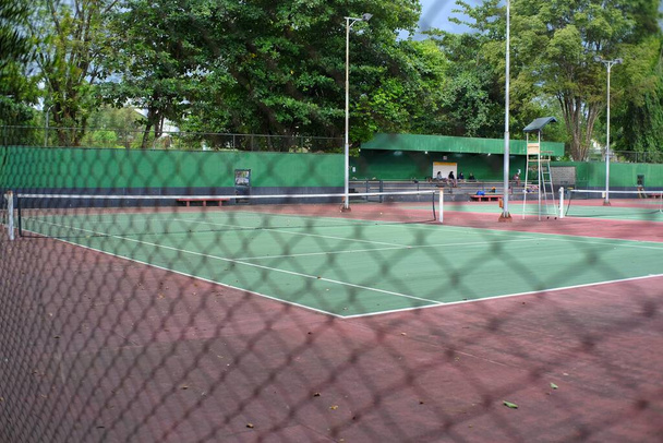 Ένα γήπεδο τένις έμεινε άδειο χωρίς ένα παιχνίδι πίσω από ένα προστατευτικό πλέγμα σύρμα - Φωτογραφία, εικόνα