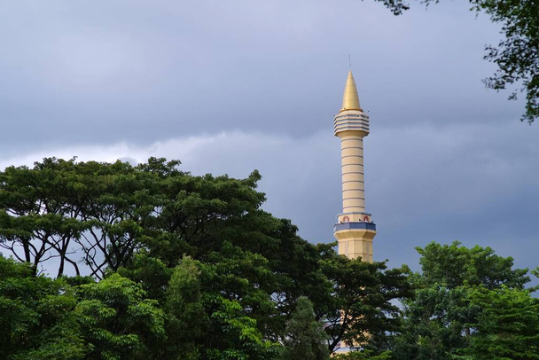 La torre della moschea che sorge in alto tra gli alberi verdi. Di solito utilizzato per posizionare altoparlanti per chiamare alla notifica di preghiera dei tempi di preghiera. - Foto, immagini