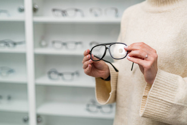 Modern eyeglasses holding by hands. Eyewear accessory in woman hands. - Фото, зображення