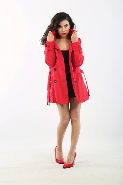beautiful young woman in a red coat and a black short dress on a white background - Photo, image
