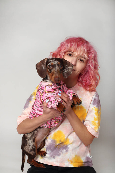 Ein Mädchen mit rosa Haaren lächelt mit einem Hund. Freunde Marmordackel. Weißer Hintergrund - Foto, Bild